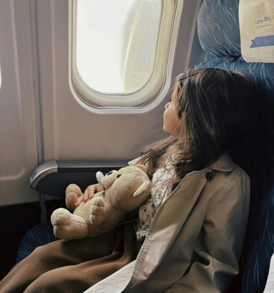 Mädchen sitzt am Fensterplatz im Flugzeug mit Teddybär, Symbolbild für Flugangst und Hypnoseunterstützung